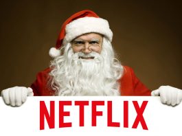 Santa Claus si appoggia in primo piano su un cartello, riportante il logo di Netflix. Il calendario Netflix di dicembre 2018 sarà ricco di regali.