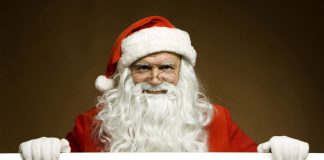 Santa Claus si appoggia in primo piano su un cartello, riportante il logo di Netflix. Il calendario Netflix di dicembre 2018 sarà ricco di regali.