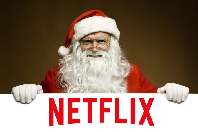 Santa Claus si appoggia in primo piano su un cartello, riportante il logo di Netflix. Il calendario Netflix di dicembre 2018 sarà ricco di regali.