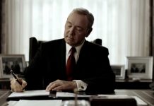 Il presidente Underwood è seduto alla scrivania dello studio ovale. Indossa un completo nero e una cravatta rossa. L'espressione è quella della soddisfazione, mentre firma un editto con una postura piena di sé. E' uno dei tratti distintivi del protagonista di House of Cards
