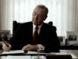 Il presidente Underwood è seduto alla scrivania dello studio ovale. Indossa un completo nero e una cravatta rossa. L'espressione è quella della soddisfazione, mentre firma un editto con una postura piena di sé. E' uno dei tratti distintivi del protagonista di House of Cards