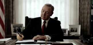 Il presidente Underwood è seduto alla scrivania dello studio ovale. Indossa un completo nero e una cravatta rossa. L'espressione è quella della soddisfazione, mentre firma un editto con una postura piena di sé. E' uno dei tratti distintivi del protagonista di House of Cards