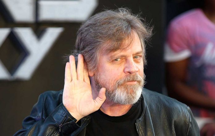 Mark Hamill tende la mano all'orecchio, con un sorrisone.