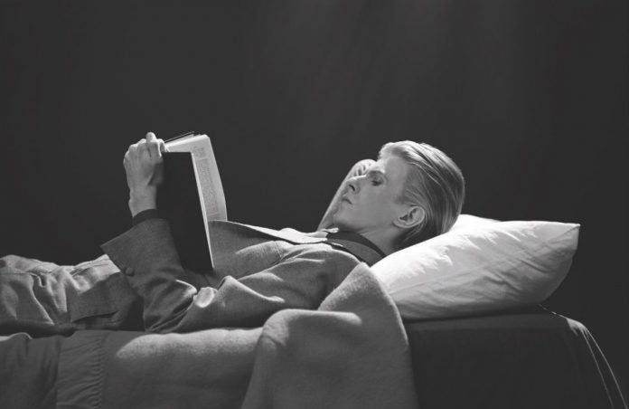 David Bowie legge disteso in una fotografia in bianco e nero, di profilo.