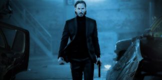 John Wick in centro ad un'immagine blu, con ai lati delle carcasse di automobili.